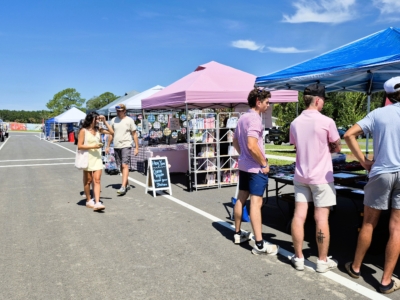 Shoppers browsing vendor tents at the Pine Royale farmers market on a sunny morning