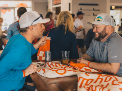 Two golfers in caps laughing over drinks at a table in the Pine Royale bar