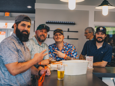 Four friends raising their beers at the bar inside Pine Royale