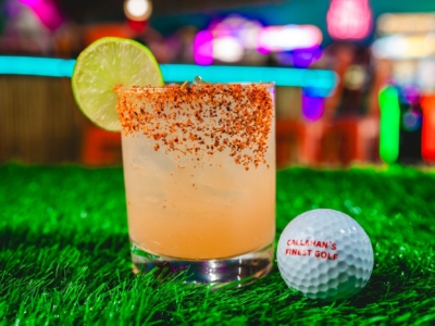 A margarita with a chili-salt rim and a lime wheel, next to a "Callahan's Finest Golf" ball