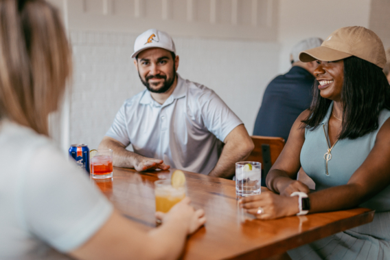 Friends smiling over drinks at a table in the Pine Royale bar