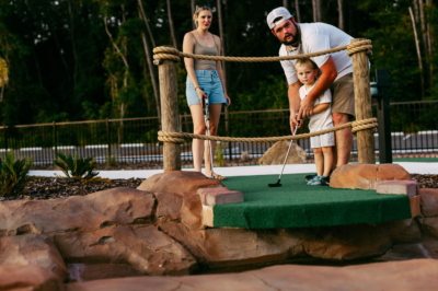 A father helping his young son putt on the rope-bridge hole at Mini Royale as mom watches