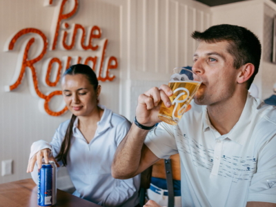 A guest sipping beer from a Pine Royale glass beside a friend in the restaurant