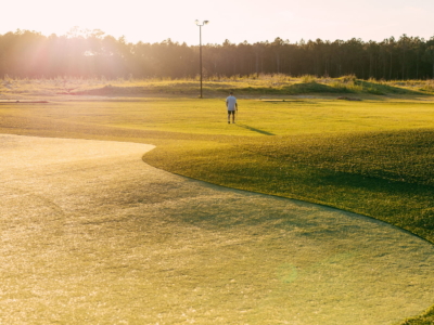 A lone golfer walking across the par 3 course at sunset