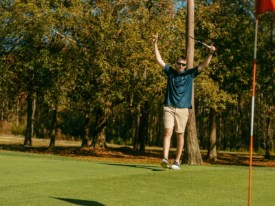 A golfer throwing his arms up in celebration on the green beside the flag