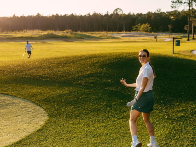 A golfer smiling back over her shoulder on the par 3 course at golden hour