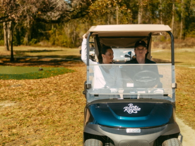 Two golfers in a Pine Royale cart driving among autumn trees