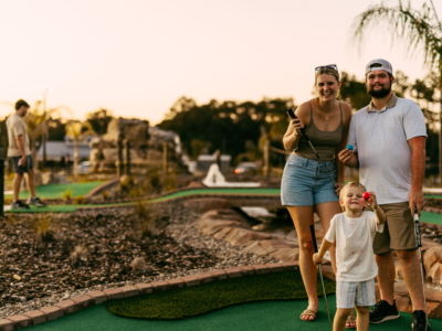 A family posing with putters on the Mini Royale course at golden hour