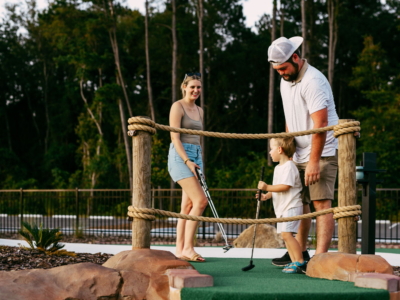 A young boy lines up a putt with his dad's help at the Mini Royale rope bridge