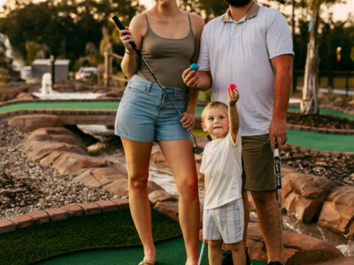 A smiling family of three holding putters and colored balls at Mini Royale