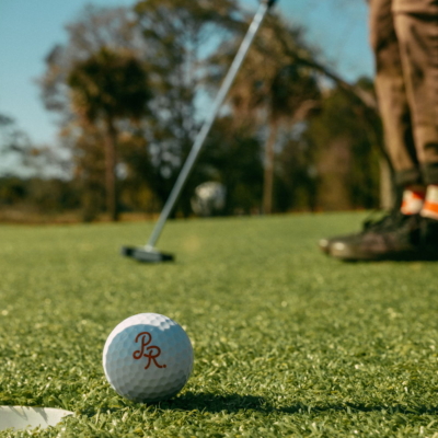 A PR-monogrammed ball beside the cup as a golfer in checkered socks putts
