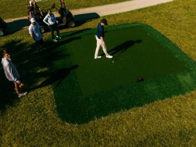 An overhead view of a golfer teeing off from a square tee box as his group watches by the carts