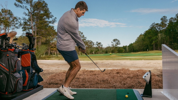 A golfer hitting from a range bay, his bag beside him and the course beyond