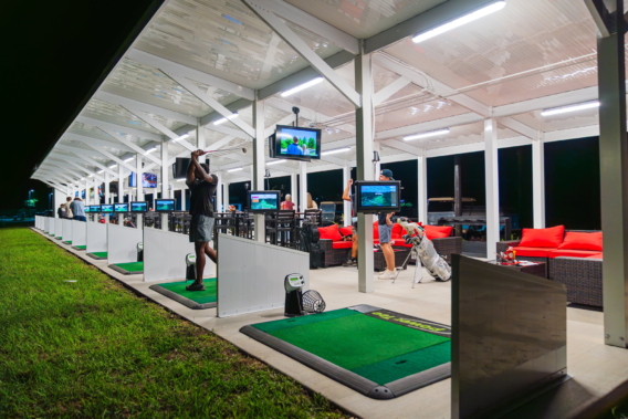 The covered driving range lit up at night, each bay with its own screen