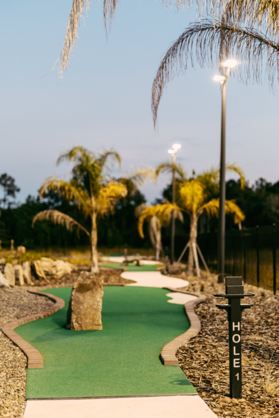 The palm-lined first hole of Mini Royale at dusk, with its hole 1 marker