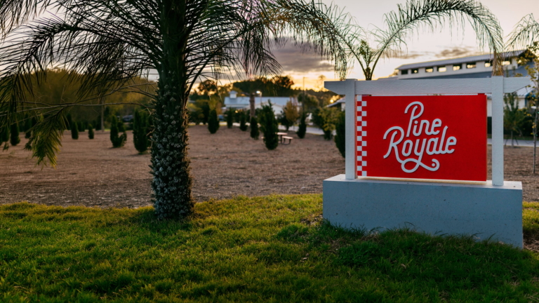 The red Pine Royale entrance sign beneath palms at sunset