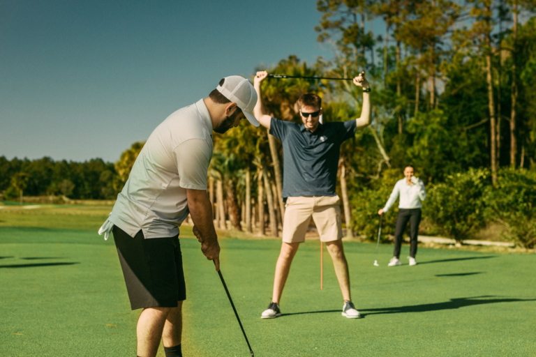 A golfer raising his club in celebration as a friend lines up a putt