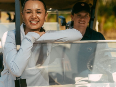 A smiling golfer leaning on the windshield of a Pine Royale golf cart