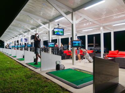 The covered driving range at night, every bay lit with its own screen, red lounge seating behind
